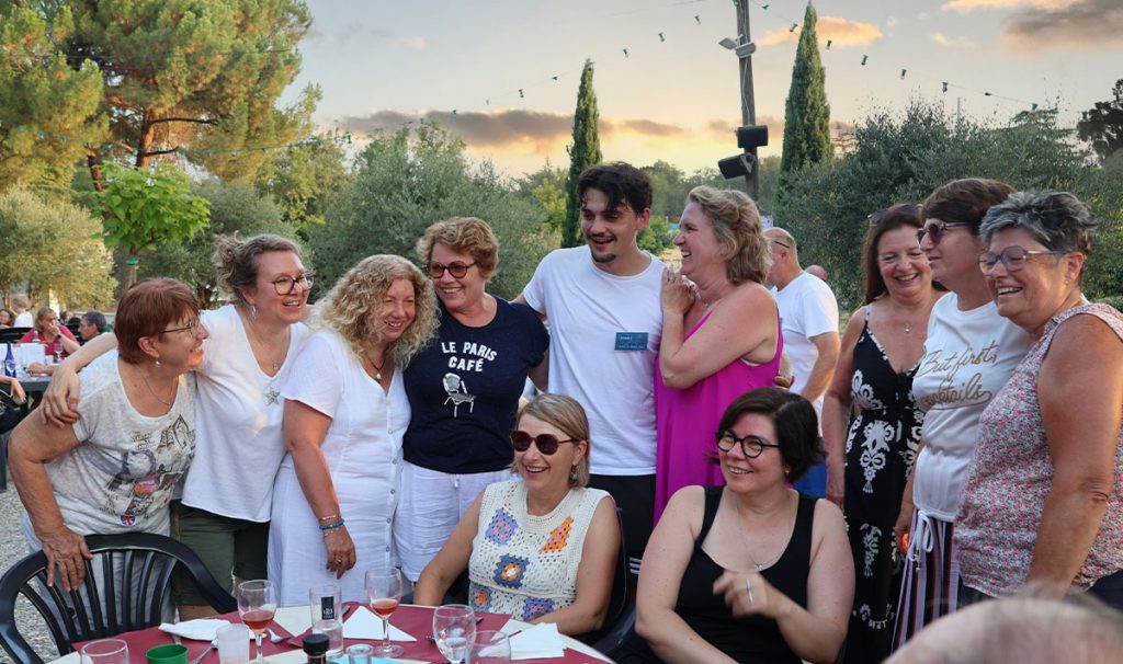 Groupe de vacanciers souriants réunis autour d’une table lors d’une soirée conviviale en plein air au Relais du Moulin Neuf