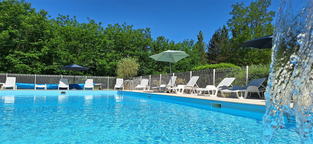 Piscine extérieure du Relais du Moulin Neuf avec transats et parasols, au cœur d’un cadre verdoyant en Lot-et-Garonne